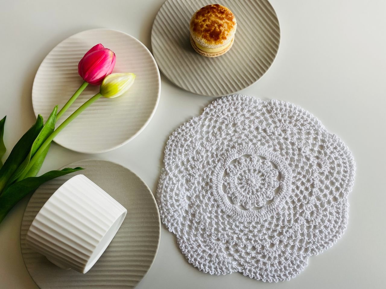 Cozy table setup with tulips, pastries, and a decorative lace mat for a serene ambiance.